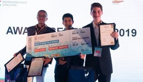 The top three learners of the 2019 Allan Gray Entrepreneurship Challenge on stage, holding certificates and an oversized grand-prize cheque for a trip to Marina Bay, Singapore. Left to right: Lazola Simane, Sachin Mohan, Kai Lemel.