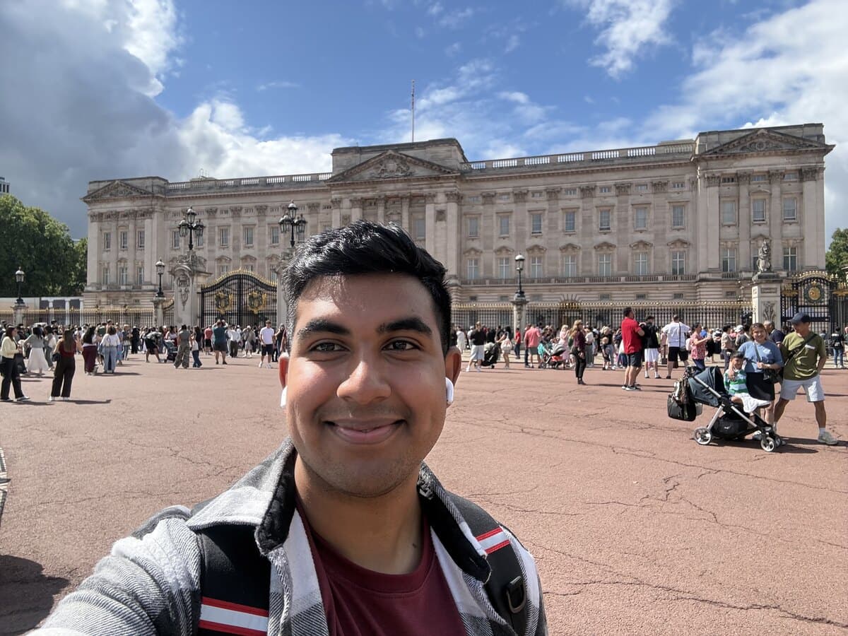 Sachin taking a selfie in front of Buckingham Palace on a bright day, crowds of tourists behind him.