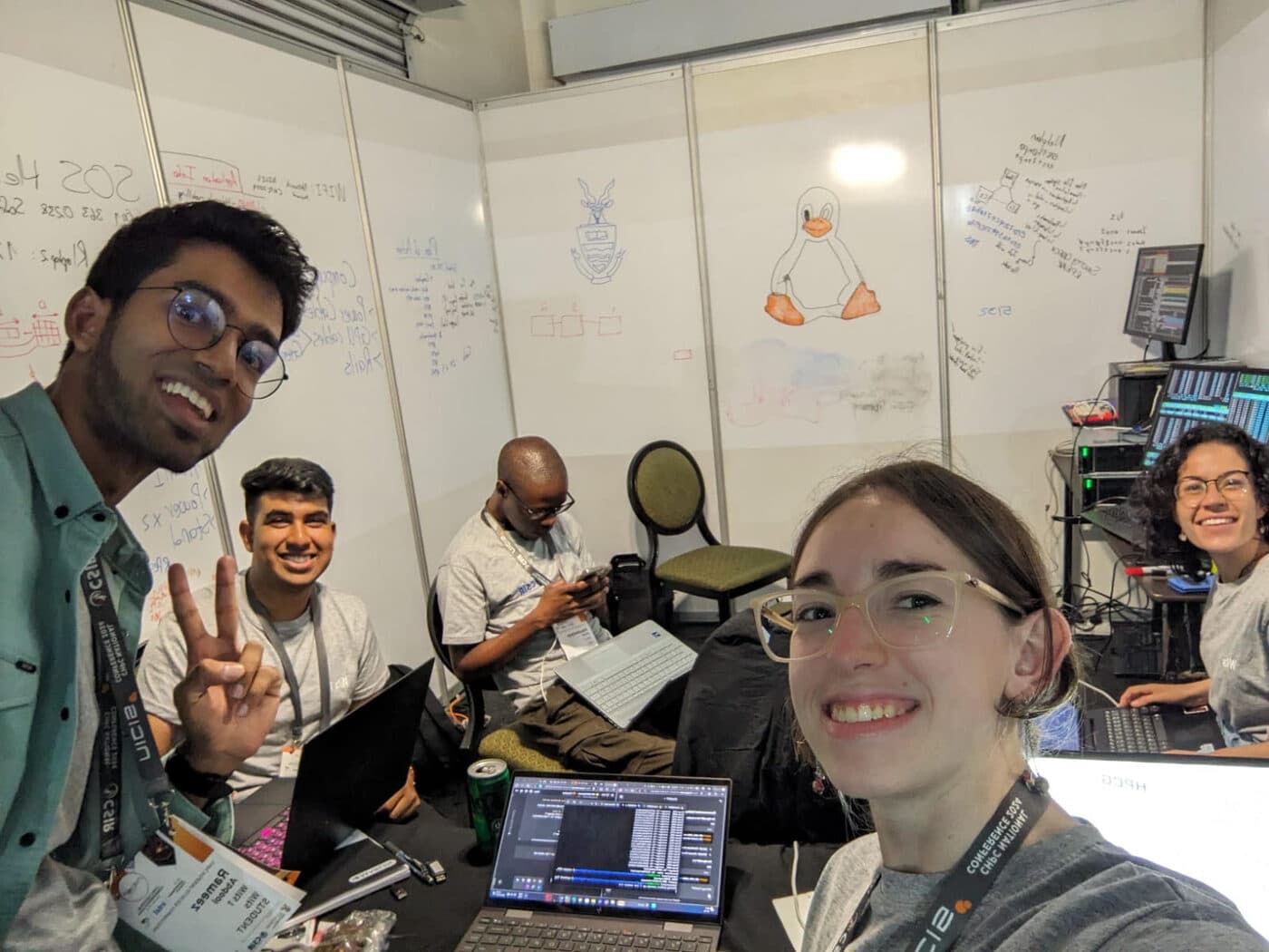 The Wits team at their CHPC competition booth, whiteboards behind them covered in network diagrams, a Wits crest and a hand-drawn Linux penguin.
